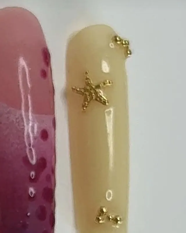 Ongle carré crème avec une étoile de mer dorée et des petites perles dorées.