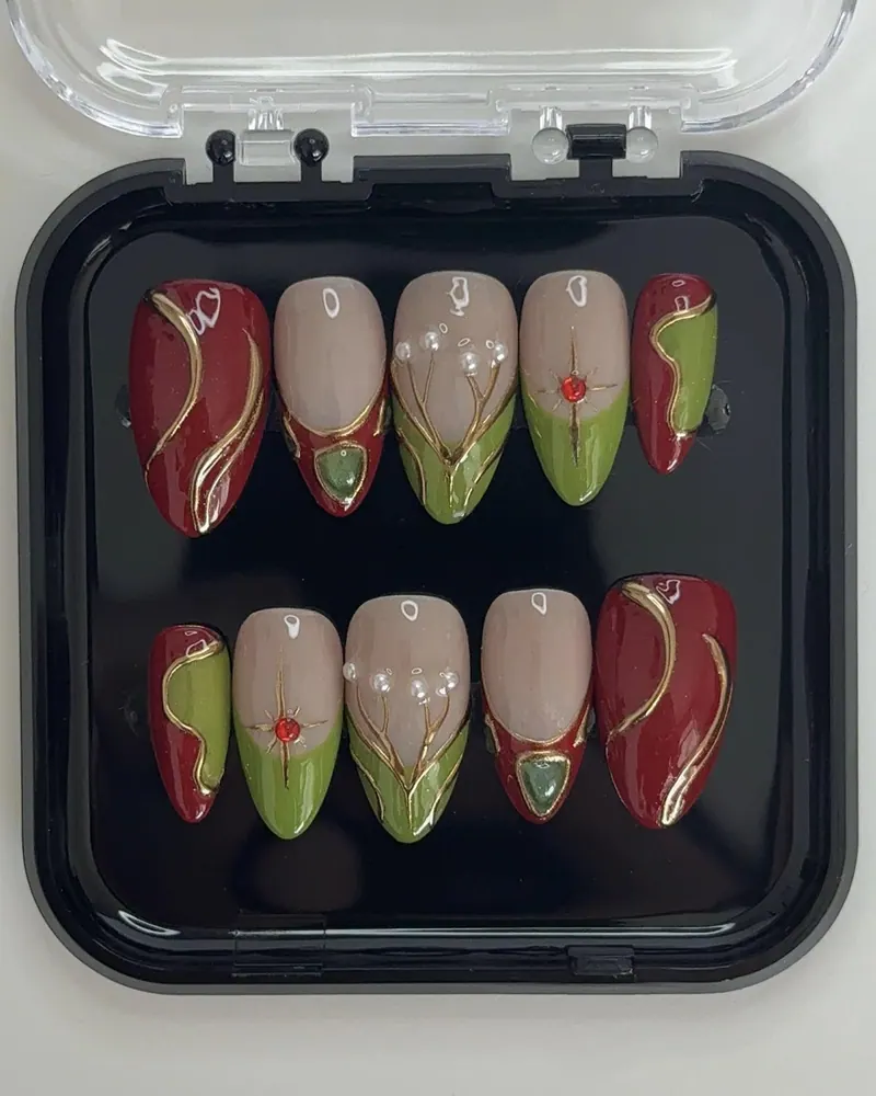 Le set dans sa boîte : ongles amande bordeaux, nude et vert, filets dorés, perles et pierres.
