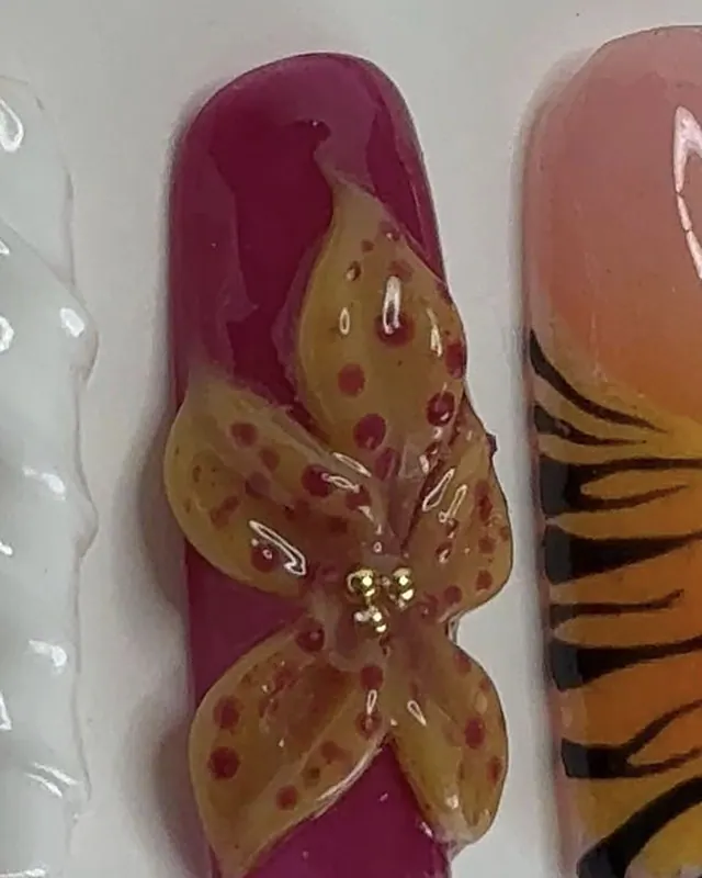Ongle carré fuchsia avec une orchidée jaune en relief, tachetée de rouge, perles dorées au centre.
